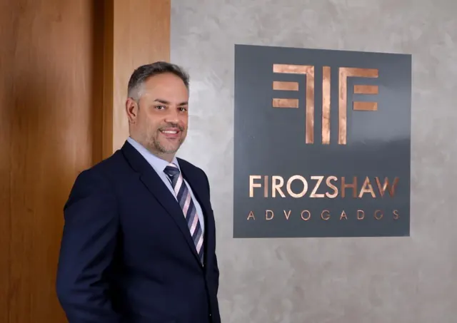 Sócio fundador do Firozshaw Advogados ao lado da marca do escritório